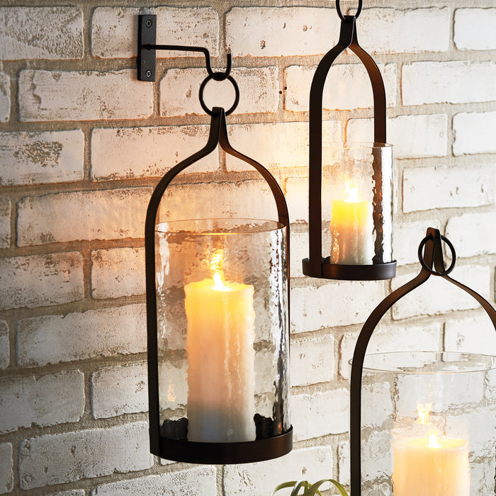Three black metal lanterns with curved top frame and frosted glass cylinders housing pillar candles, mounted near a white