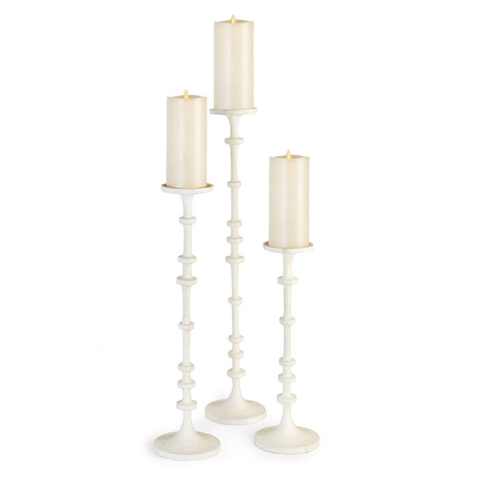 A set of three white aluminum candle stands with a notched design on the base, displaying three lit candles on top.