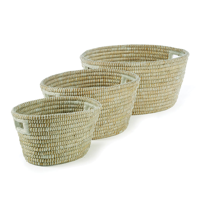 A set of three oval-shaped wicker baskets with handles, in a natural beige color.