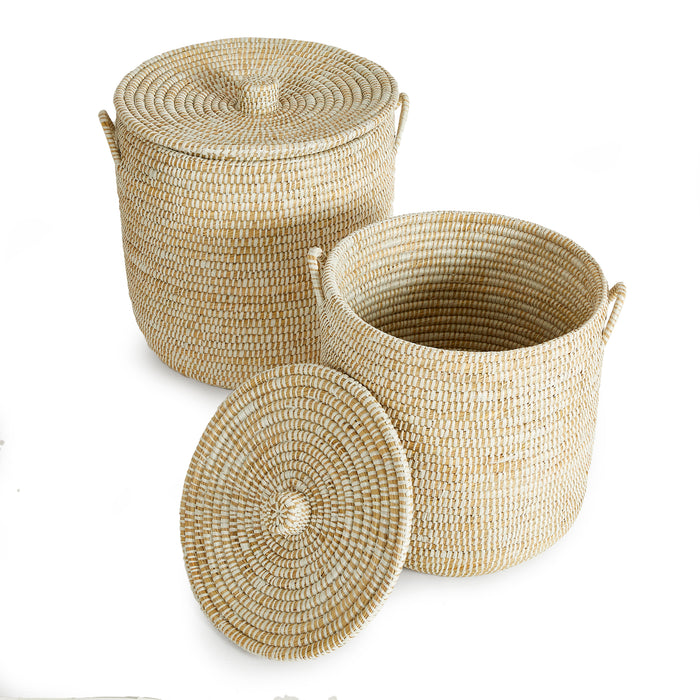 Two woven straw hampers with lids; natural beige color, round shapes, included lid in foreground, white background.