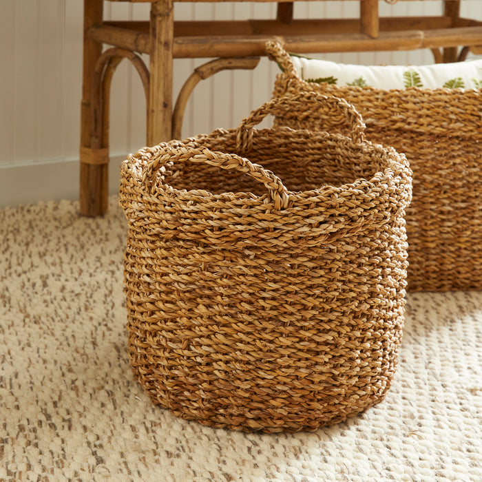 Seagrass oval basket set of three with two handles, natural woven texture on beige rug in sunlit room.