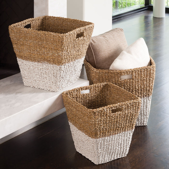 Set of three woven rectangular baskets in natural tan and white tones, two with handles and one filled with cushions, placed