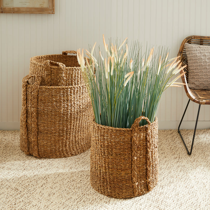 Three seagrass round baskets in natural brown tones, large set with braided handles, one filled with tall ornamental