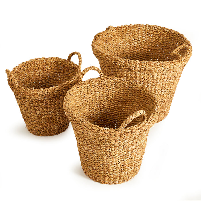 Set of three tapered seagrass baskets with handles in natural brown woven texture, empty, against white background.
