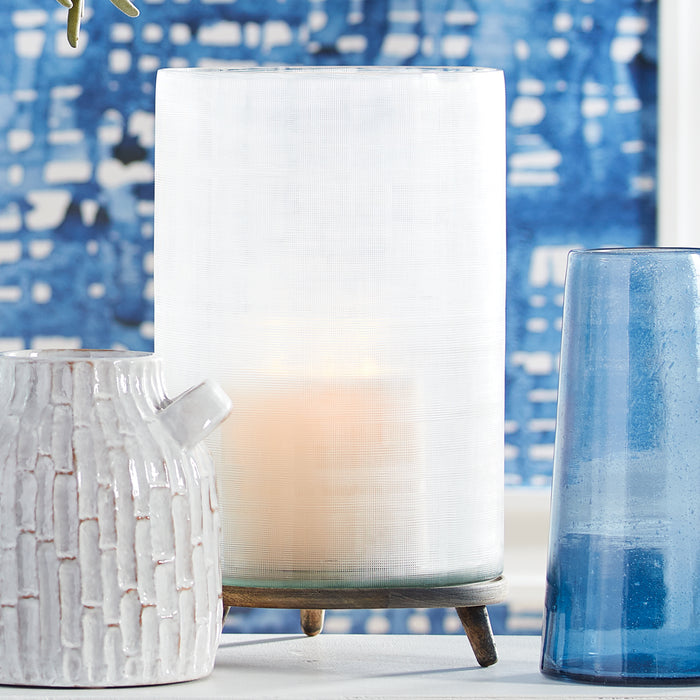 White cylindrical lampshade with wooden base, glowing softly, flanked by a textured white ceramic pitcher and a tall blue
