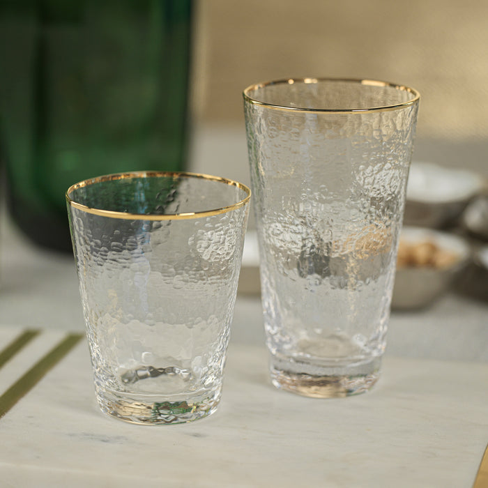 Two clear glasses with gold rims on a light surface.