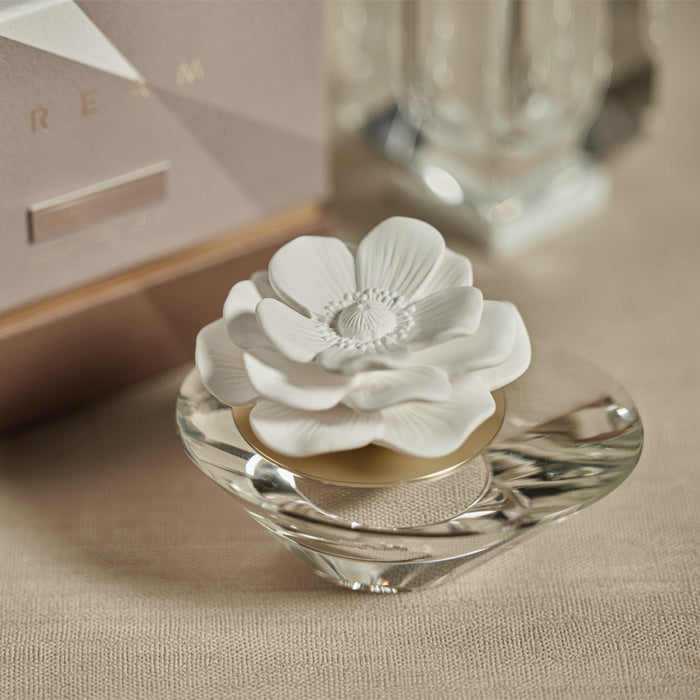 An elegant white porcelain flower diffuser placed on a crystal-like surface, with a soft focus background.