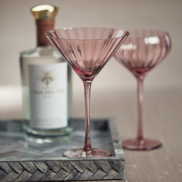 Set of four pink martini glasses with long stems and fluted bowls, shown on a metal tray with a bottle of liquor in