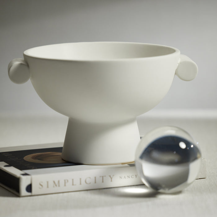 White ceramic bowl with spherical handles on a book titled 'Simplicity'.
