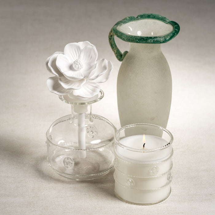 Decorative glass items including a flower-shaped candle holder, a white vase, and a small glass container with a candle on a neutral background.