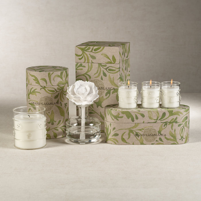 Beige diffuser set with green leaf-patterned boxes and glass bottle; ivory candles in silver-rimmed glass holders; elegant