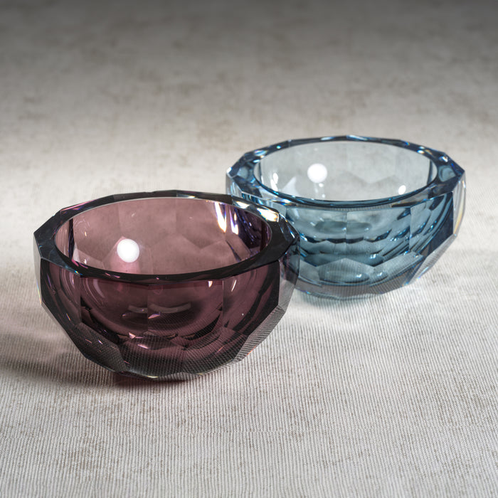 Two glass bowls, one purple and one blue, on a beige surface.