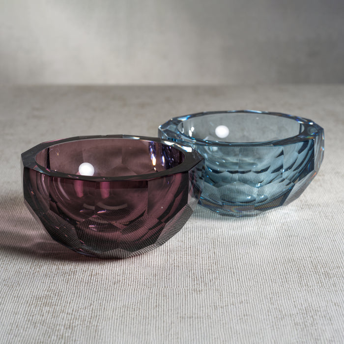 Two glass bowls, one purple and one blue, on a textured surface.