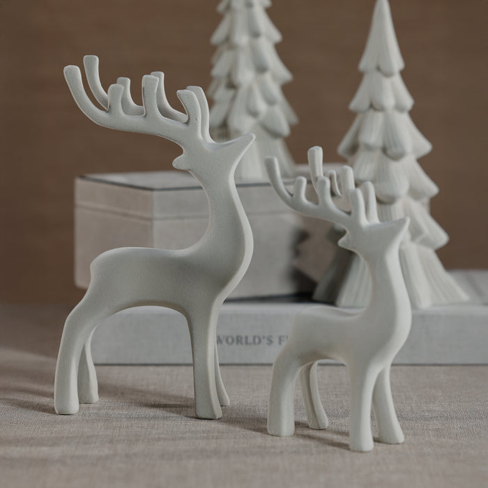 White ceramic deer figurines with a blurred background of books and trees.