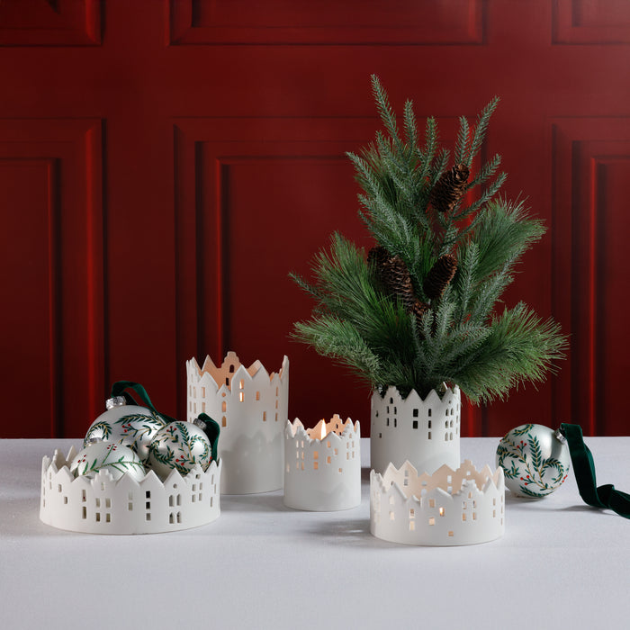 Decorative candles and a small tree with pine cones against a red wall.