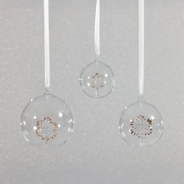 Three clear spherical ornaments with floral designs inside, hanging on a gray background.