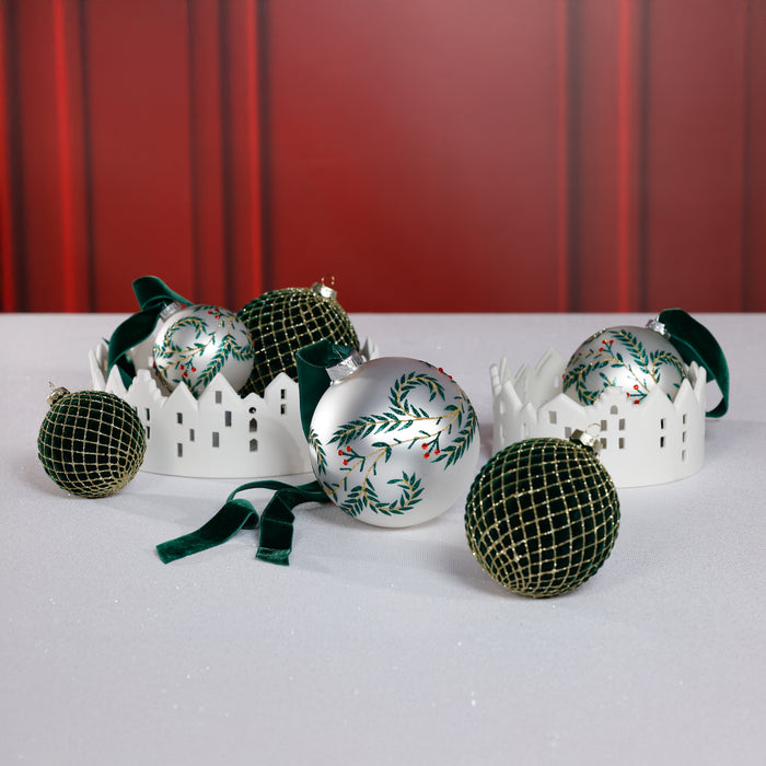 Decorative Christmas ornaments with green and silver designs on a white surface against a red curtain background.