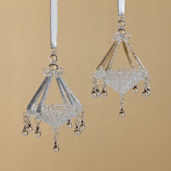 Two silver chandelier-shaped ornaments on a beige background