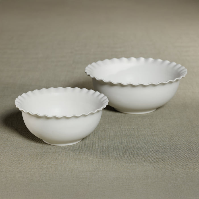 Two white ceramic bowls with scalloped edges on a beige fabric background
