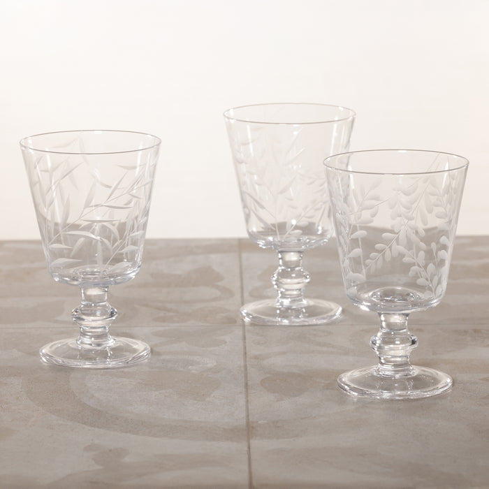 Three clear glass goblets with etched designs on a light gray surface.