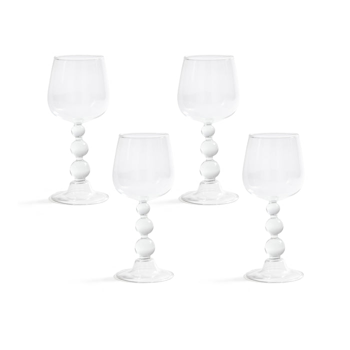Four white wine glasses with decorative stems on a white background