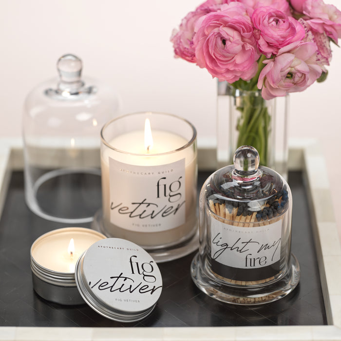 Fig and vetiver candles with matches and a vase of pink flowers on a tray.