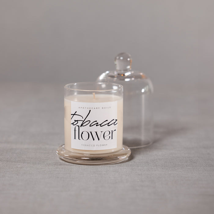 Candle labeled 'tobacco flower' with a glass cover on a gray surface