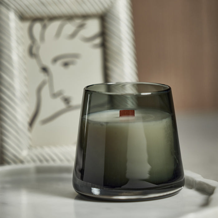 Dark green apothecary-style candle jar with a white wax interior and a brown wick, on a white marble surface with a framed
