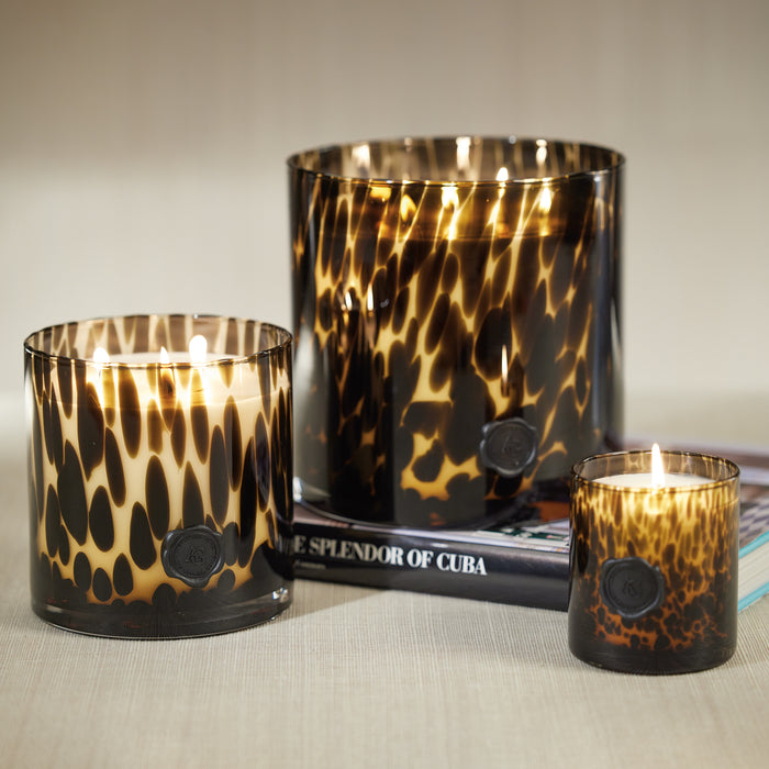 Three candles with black and brown marbled glass jars, two larger and one smaller, set on a surface with a book in the background.