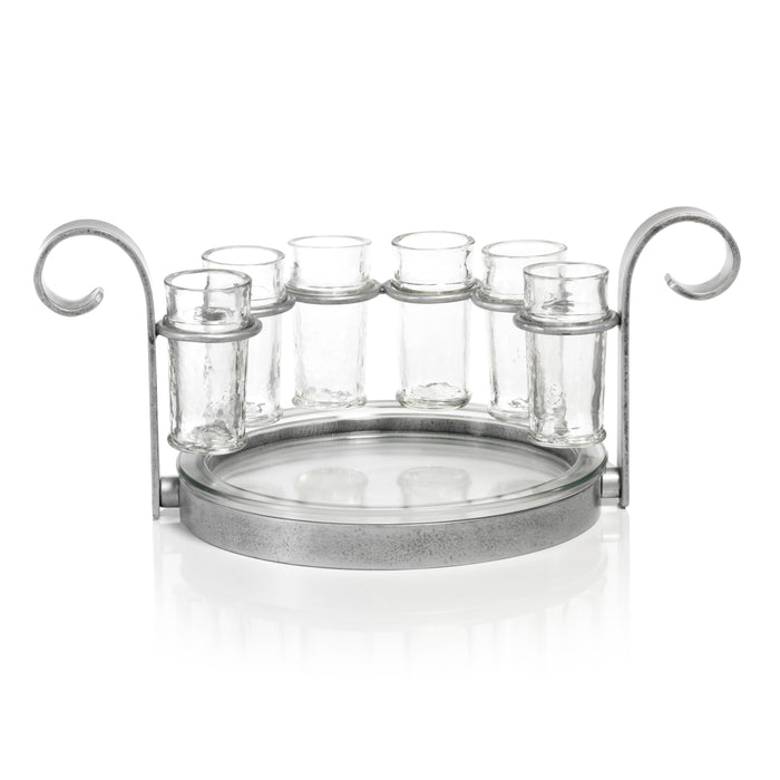 A set of six clear glass shot glasses arranged in a silver metal stand with a glass tray below.