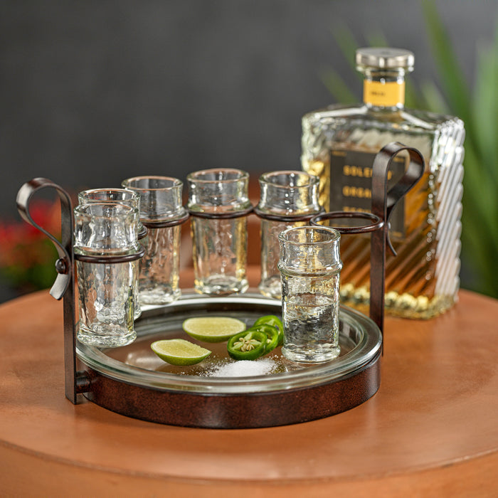 Set of shot glasses on a tray with a bottle of tequila in the background