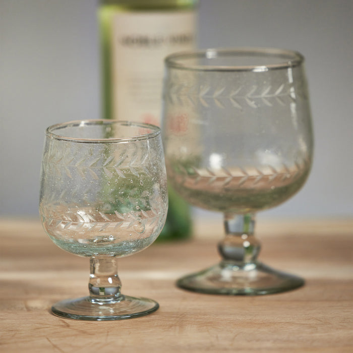 Two etched clear wine glasses with short stems on a wooden surface, blurred bottle in background.