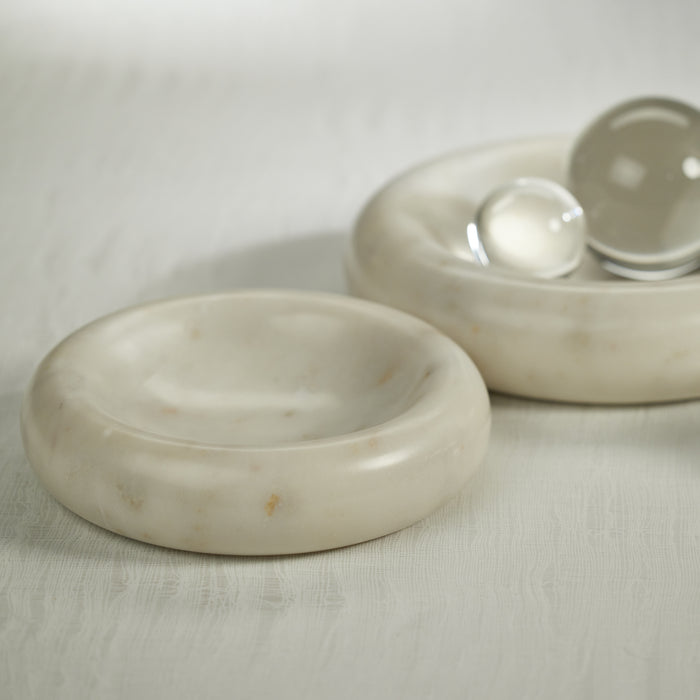 A white curved round marble bowl on a wooden surface with a glass ball inside it.