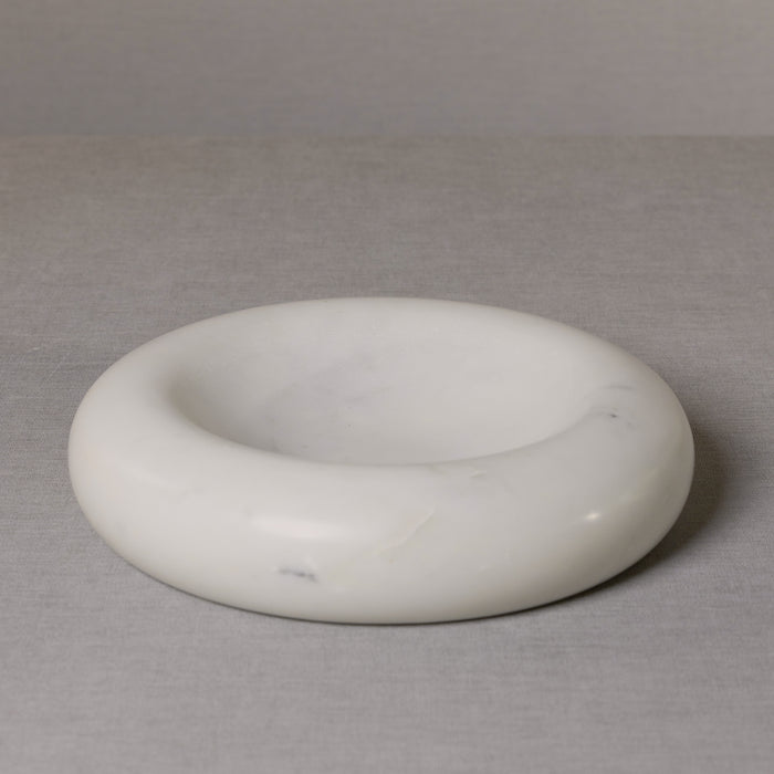 Large round white marble bowl with curved inner well, smooth polished surface, subtle gray veining, on gray fabric