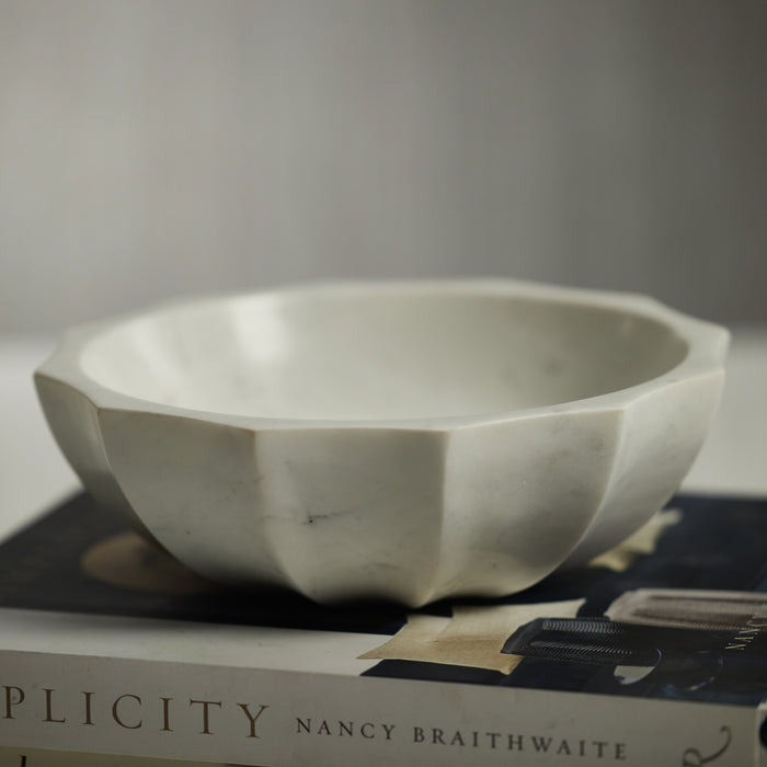 A white marble bowl with a scalloped design, placed on a book.