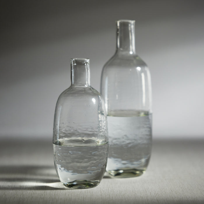 Two clear glass decanters with a hammered texture, one smaller and one larger, filled with water, set against a neutral background.