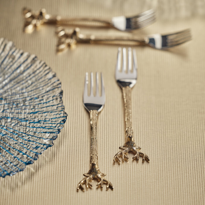 A set of four hors d'oeuvre forks with reindeer-shaped handles, placed on a table with a decorative plate in the background.
