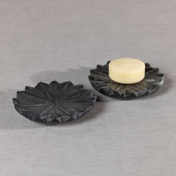 Two dark gray lotus-shaped marble dishes, one coin placed on top of the other, light beige soap on the back dish, neutral
