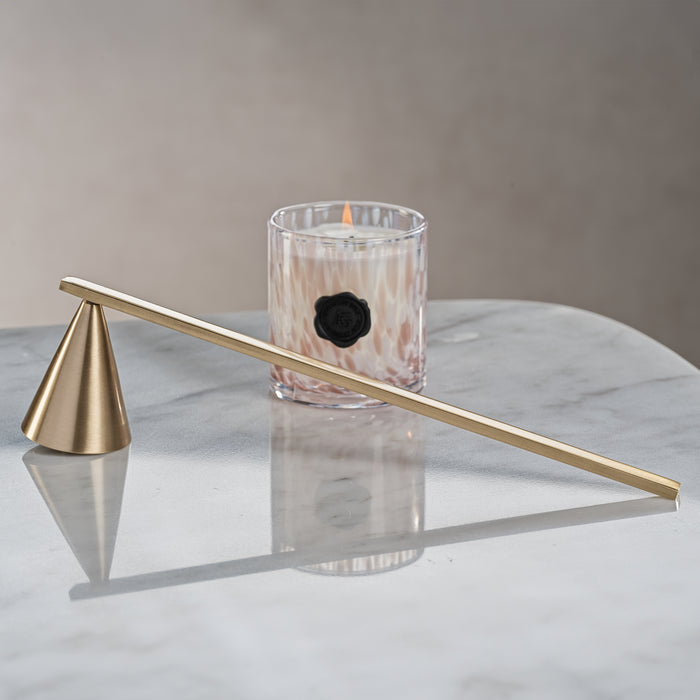 Gold candle snuffer on a marble surface with a lit candle in the background