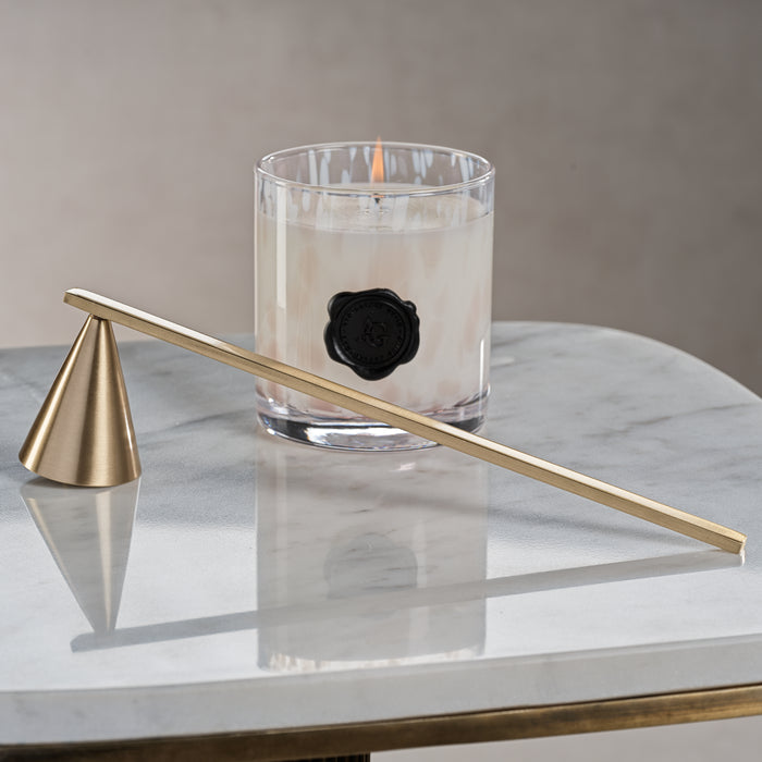 Gold candle snuffer in front of a lit candle with a black rose on a marble surface.