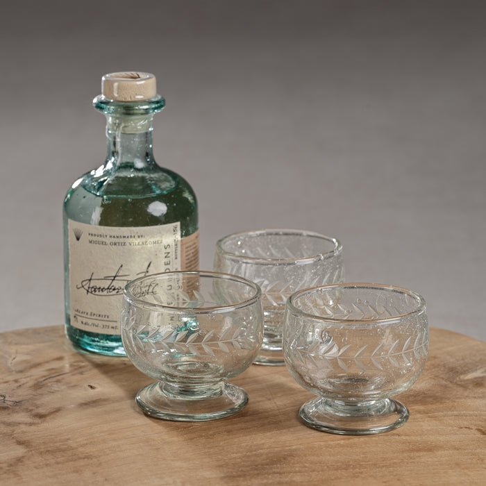 Vintage-style bottle with cork stopper and four glass tumblers on a wooden surface.