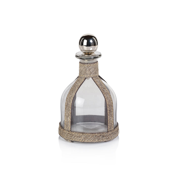 A clear glass decanter with a gray hair-on-hide leather wrap and a brass metal stopper.