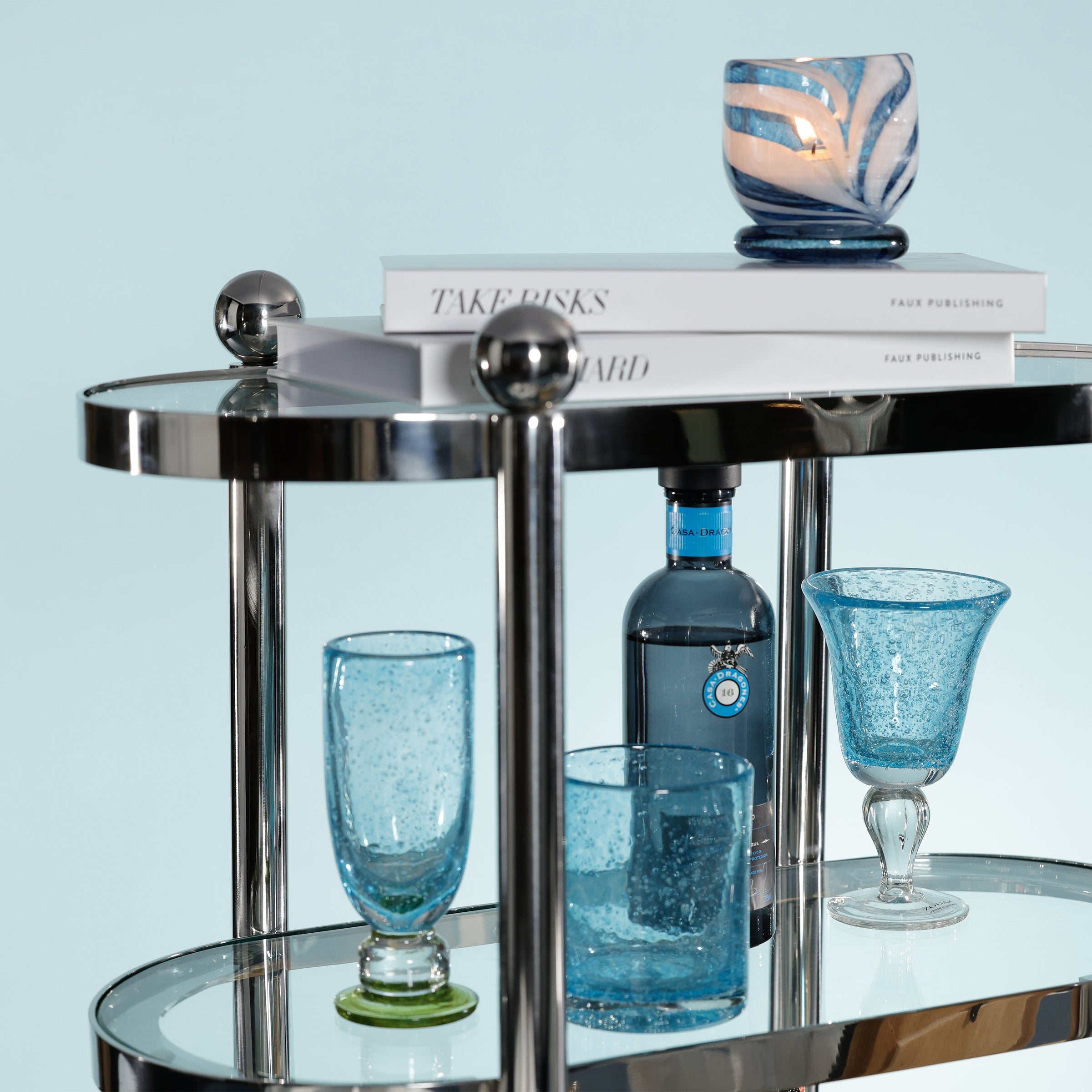 Glass bar cart with blue glasses and a bottle on a light blue background