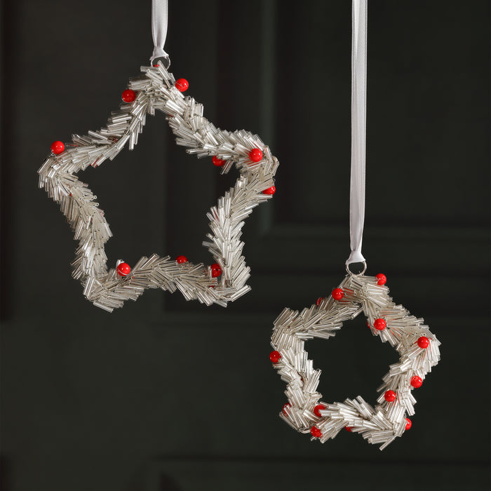 Two star-shaped Christmas decorations with red berries on a black background