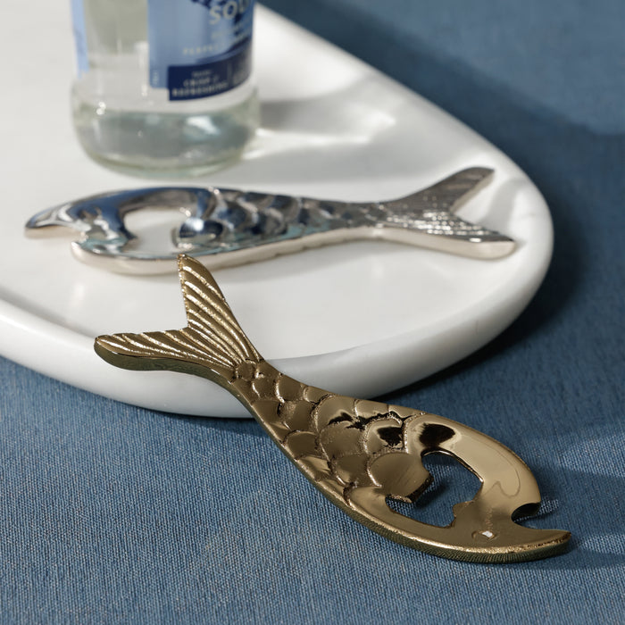 Gold and silver fish-shaped bottle openers on a white tray with a blue background