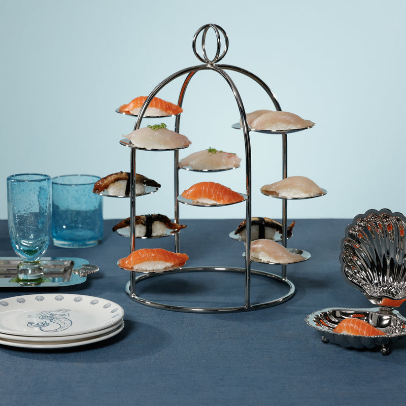 Three-tiered metal stand with various types of sushi on a blue tablecloth.