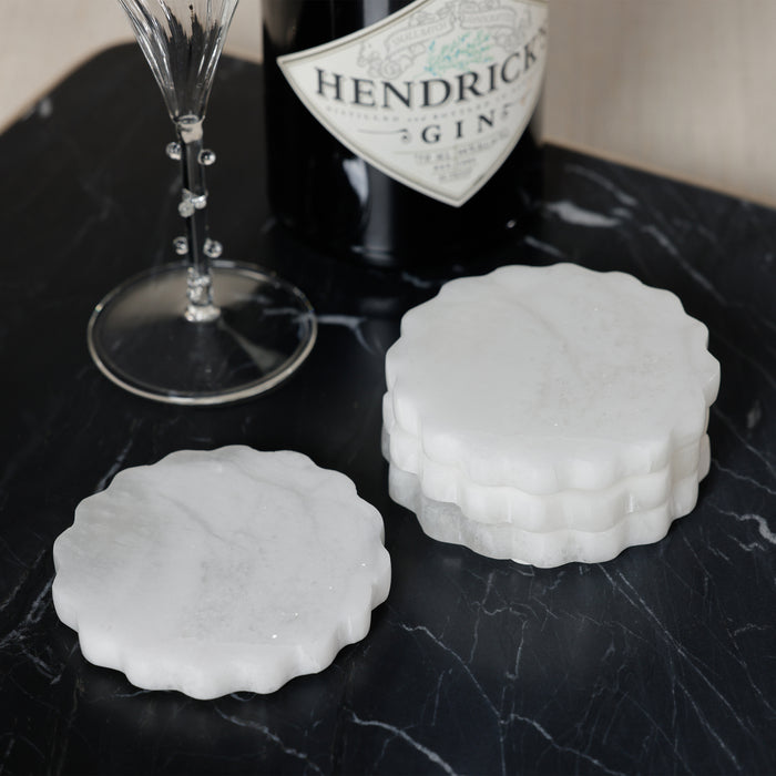 Two white marble coasters on a black marble surface with a bottle of Hendrick's gin and a glass.