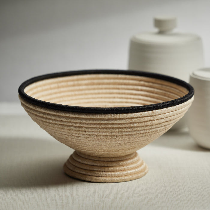 Beige woven bowl with black rim on a neutral background
