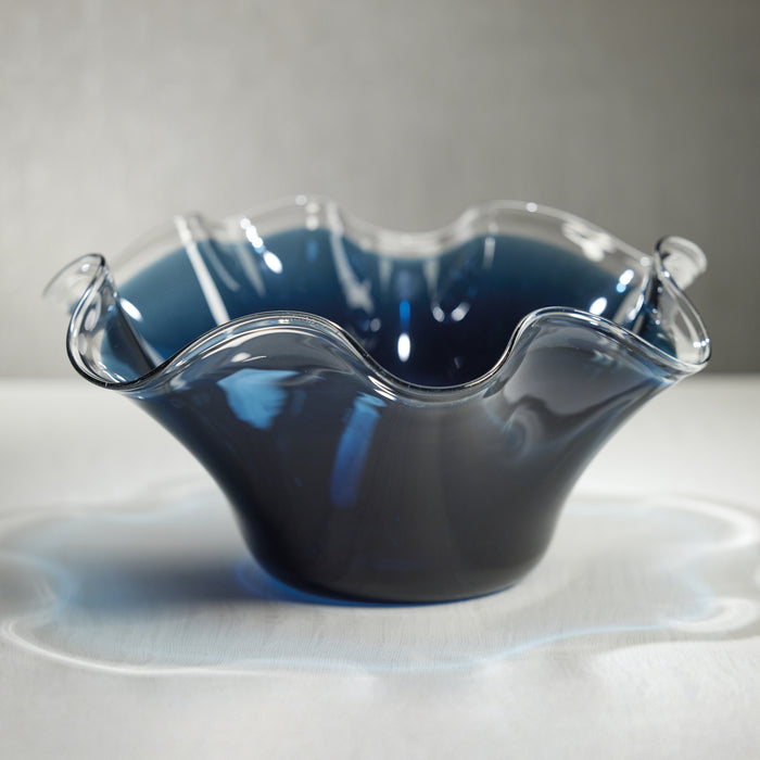 Clear glass bowl with wavy design filled with dark blue liquid on a light gray background