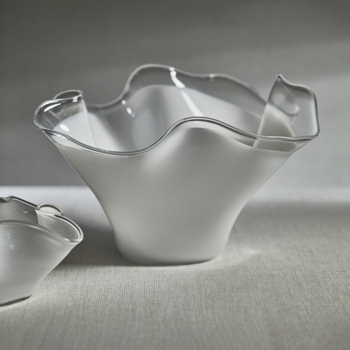 A white, wave-shaped glass bowl on a textured surface, with a smaller bowl partially visible in the background.